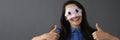 Smiling woman in mask on face holds thumbs up