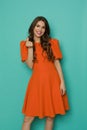 Smiling woman in orange mini dress is showing mini-heart finger hand sign gesture