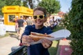 Smiling woman at an outdoor fair holds up a half-eaten footlong hot dog. Focus on the hot dog, girl intentionally blurred