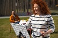 Smiling woman painting picture on easel outdoors