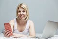 A smiling woman in pajamas lies on her stomach in bed with a laptop and a smartphone. Blogging and telework during the coronavirus Royalty Free Stock Photo