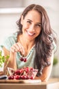 Smiling woman picks two cherries from a seethrough bowl indoors