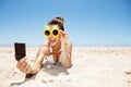 Smiling woman in pineapple glasses taking selfie at sandy beach