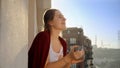 Smiling woman with plaid drinking coffee on balcony at morning. People relaxing, resting at home, beautiful cityscape Royalty Free Stock Photo