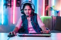 Smiling woman playing video game by talking on headphones while looking at camera at neon background - concept of Royalty Free Stock Photo