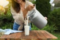 Smiling woman pouring fresh milk from can into glass at wooden table outdoors Royalty Free Stock Photo