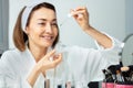 Smiling woman putting facial serum with eyedropper on the face