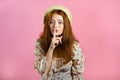 Smiling woman with red hair holding finger on her lips over pink background. Gesture of shhh, secret, silence. Close up. Royalty Free Stock Photo