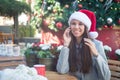 Smiling woman in Santa hat talking on her phone in cafe outside Royalty Free Stock Photo