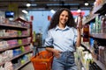 Smiling woman shopping in supermarket aisle holding bottle and basket Royalty Free Stock Photo