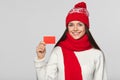 Smiling woman showing blank credit card, winter concept. Happy girl in red hat and scarf holding card, isolated over gray Royalty Free Stock Photo
