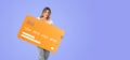 Happy woman standing with mock up credit card on empty purple background