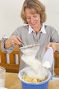 Smiling woman sieving flour into dough