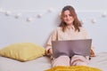 A smiling woman sits with a laptop and works on a white bed. Happy girl with a computer in the bedroom, close-up Royalty Free Stock Photo