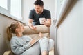 Smiling woman sitting on beige armchair and brunet man standing beside her on balcony