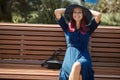 Smiling woman sitting on bench in park. Cute lady in hat and blue dress. Leisure time, take break and new emotion idea