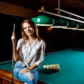 Smiling woman sitting on billiards table with cue.