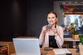 Smiling woman sitting in cafeteria holding coffee mug and working on laptop Royalty Free Stock Photo