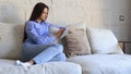 Smiling woman sitting on sofa with digital tablet and chating with friends.