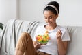 Smiling woman sitting on sofa at home, eating healthy food Royalty Free Stock Photo
