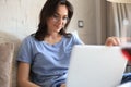 Smiling woman sitting on sofa with laptop computer and chating with friends
