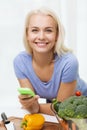 Smiling woman with smartphone cooking vegetables