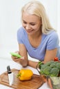 Smiling woman with smartphone cooking vegetables