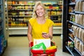 Smiling woman with smartphone pushing trolley in aisle Royalty Free Stock Photo