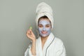 Smiling woman spa model in moisturizing cosmetic face mask with cucumber on white background. Female in white bathrobe and towel.