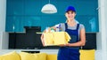 Smiling woman in special uniform for cleaning apartment holds the box with detergents, gloves, rags and standing in