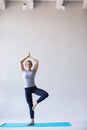 Smiling woman in sportswear practicing yoga, standing in Vrksasana exercise with namaste, Tree pose on gray background. Royalty Free Stock Photo
