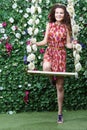 Smiling woman stands next swing overgrown with flowers