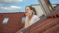 Smiling woman talking on her phone while gazing out of an open attic window, taking in the picturesque sight of red Royalty Free Stock Photo