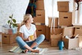 Woman with tea in hand sitting on floor of new apartment, pile of moving boxes on background Royalty Free Stock Photo