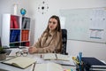 Smiling woman teacher sitting at desk with laptop and explaining grammar rules near whiteboard Royalty Free Stock Photo