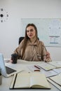 Smiling woman teacher sitting at desk with laptop and explaining grammar rules near whiteboard Royalty Free Stock Photo