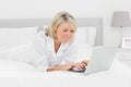 Smiling woman using her laptop on her bed Royalty Free Stock Photo