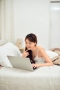 Smiling woman using a laptop while lying on her bed Royalty Free Stock Photo