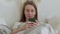 Smiling woman using a mobile phone was lying on the bed. Happy brunette young woman uses mobile phone at home. Royalty Free Stock Photo