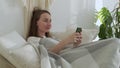 Smiling woman using a mobile phone was lying on the bed. Happy brunette young woman uses mobile phone at home. Royalty Free Stock Photo