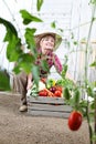 Smiling woman in vegetable garden with wooden box of vegetables