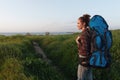 Smiling woman walking in the meadow with trekking backpack by the sea