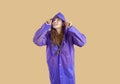 Smiling woman in purple coat peeks out of hood and looks up on yellow background, halloween concept. Royalty Free Stock Photo