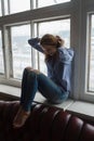 smiling woman wearing blue striped shirt and ripped jeans sitting on windowsill Royalty Free Stock Photo