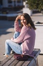 Fashionable trendy stylish young girls in cozy pink knitted sweater sitting on wooden city bench and laughing