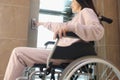 Smiling woman in wheelchair presses button of elevator