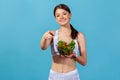 Smiling woman is white sportswear with slim body pointing finger on you holding bowl with vegetable salad, suggesting nutritional