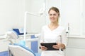 Smiling woman in white uniform holds tablet in her hands standing inside dentist office. Selective focus Royalty Free Stock Photo