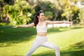 Smiling woman in white workout attire practices Warrior II pose with arms outstretched in a park Royalty Free Stock Photo