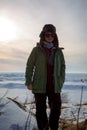 Smiling woman in winter clothes on frozen lake shore during sun